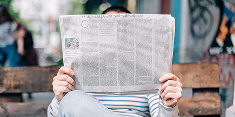 A person sitting on a bench, reading a newspaper